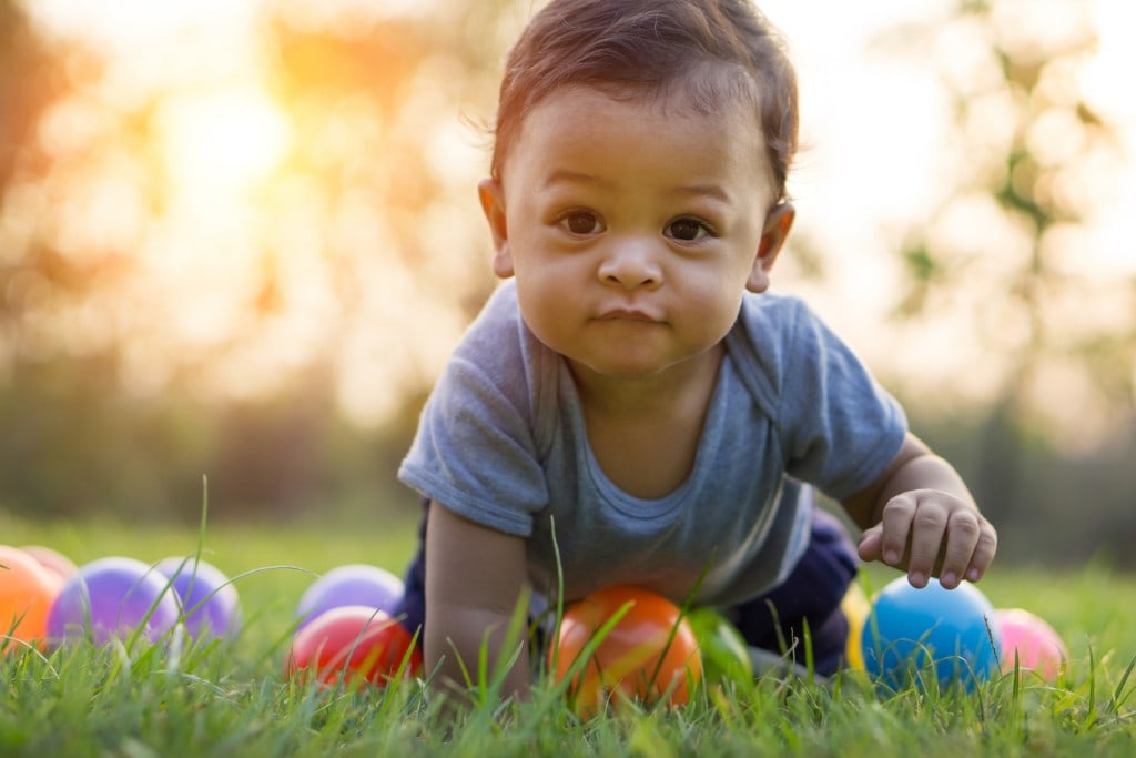 Cute asian baby crawling in the green grass and with colorful balls.