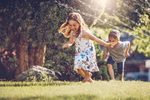 Kids happily playing with sprinkler outside.
