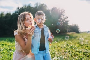 Mother and little son blowing soap bubbles in summer day.