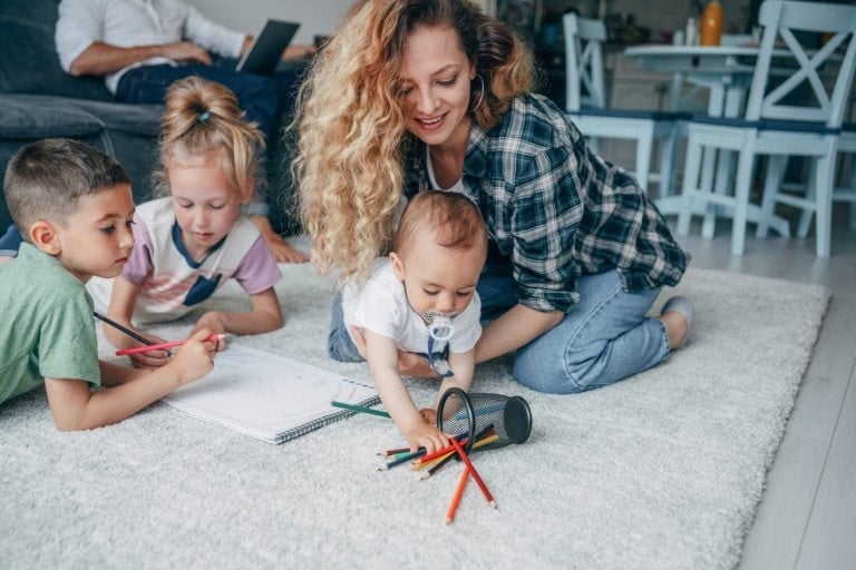 Young happy family drawing on the floor. Father working on a laptop at home.