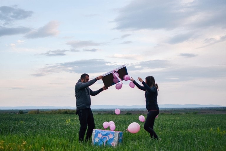Gender reveal moment where a dad and mom are opening a box and finding pink balloons inside. It's a girl!