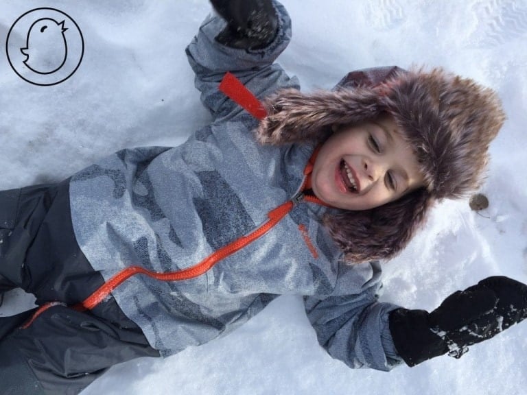 toddler smiling and laying on back in the snow