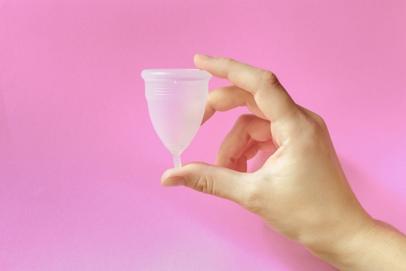 Close up of woman hand holding menstrual cup over pink background.