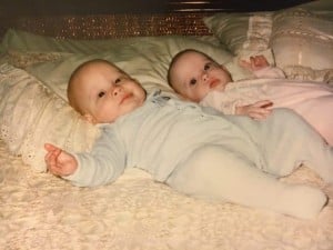Two babies lie on a bed with lace-trimmed pillows. The baby on the left, clad in a light blue outfit, and the baby on the right, dressed in pale pink, share calm expressions. Their peaceful demeanor brings to mind what we've learned from autism about finding serenity in simple moments.