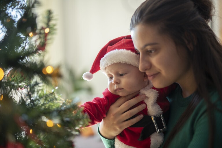 Mother and baby son decorating tree for baby's first Christmas celebration.
