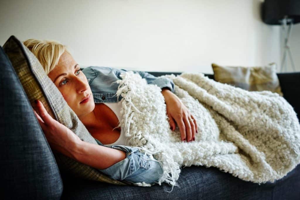 Pregnant woman laying on couch covered with a blanket.
