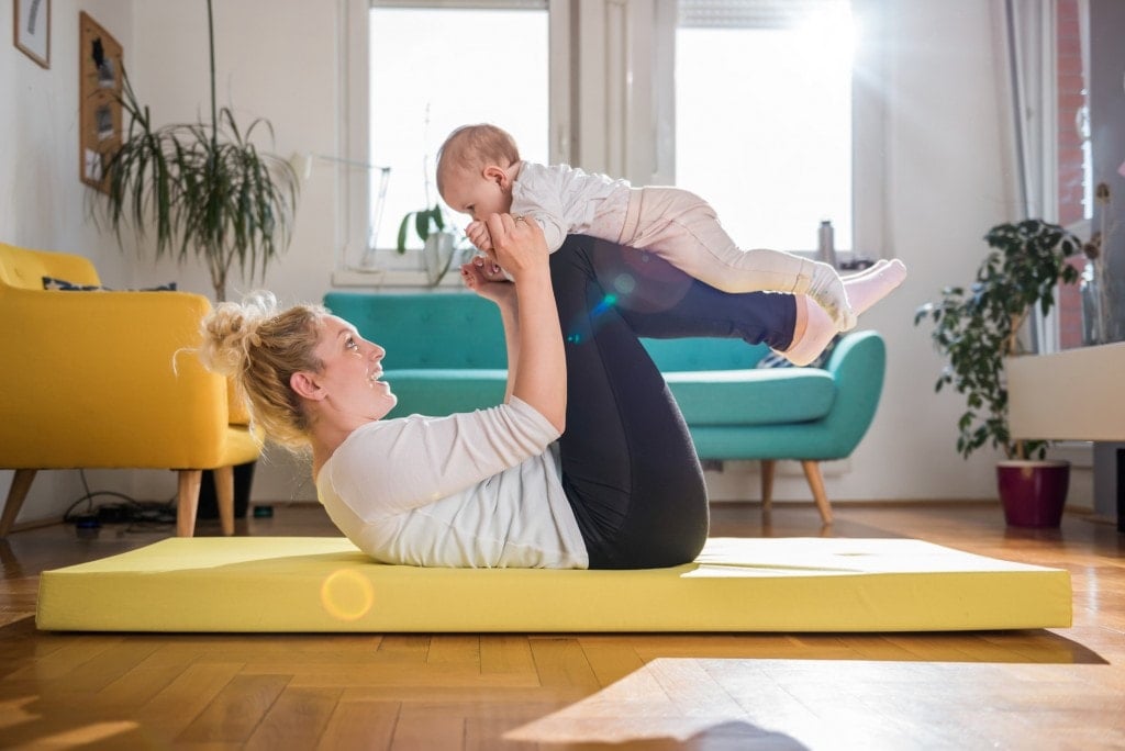 Mother Exercise With Her Baby on yellow mat At Home