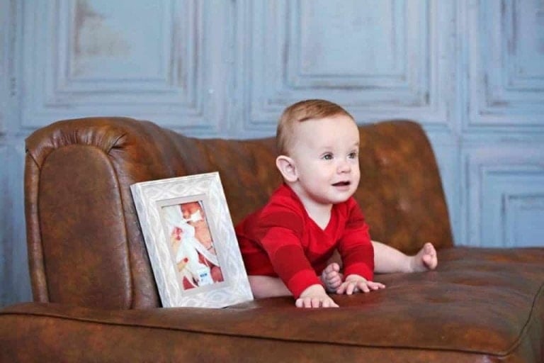 Baby on couch next to picture of when he was in the NICU.