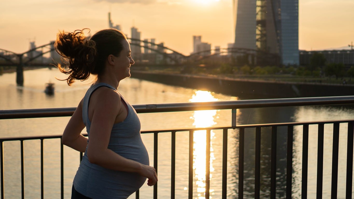 Active pregnant woman running across the bridge with a beautiful view of the city of Frankfurt in Germany