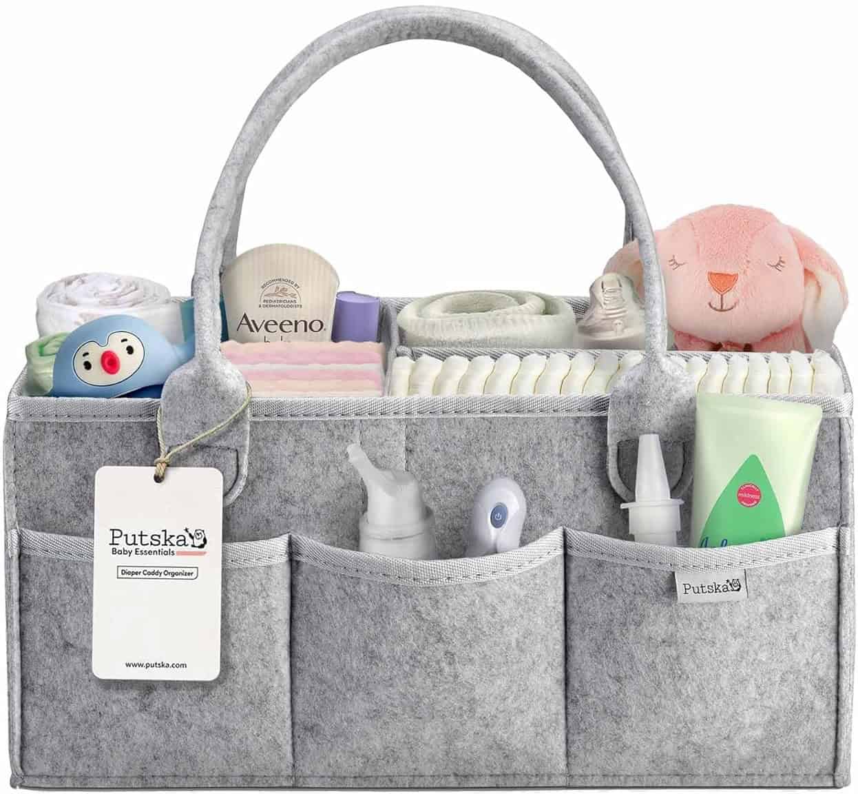 A grey felt baby caddy organizer is pictured containing various baby care items, perfect for those looking for DIY baby shower gifts. It includes a small pink stuffed toy, a pacifier, a bottle of lotion, a thermometer, a nasal aspirator, a tube of cream, diapers, baby wipes, and a baby bib.