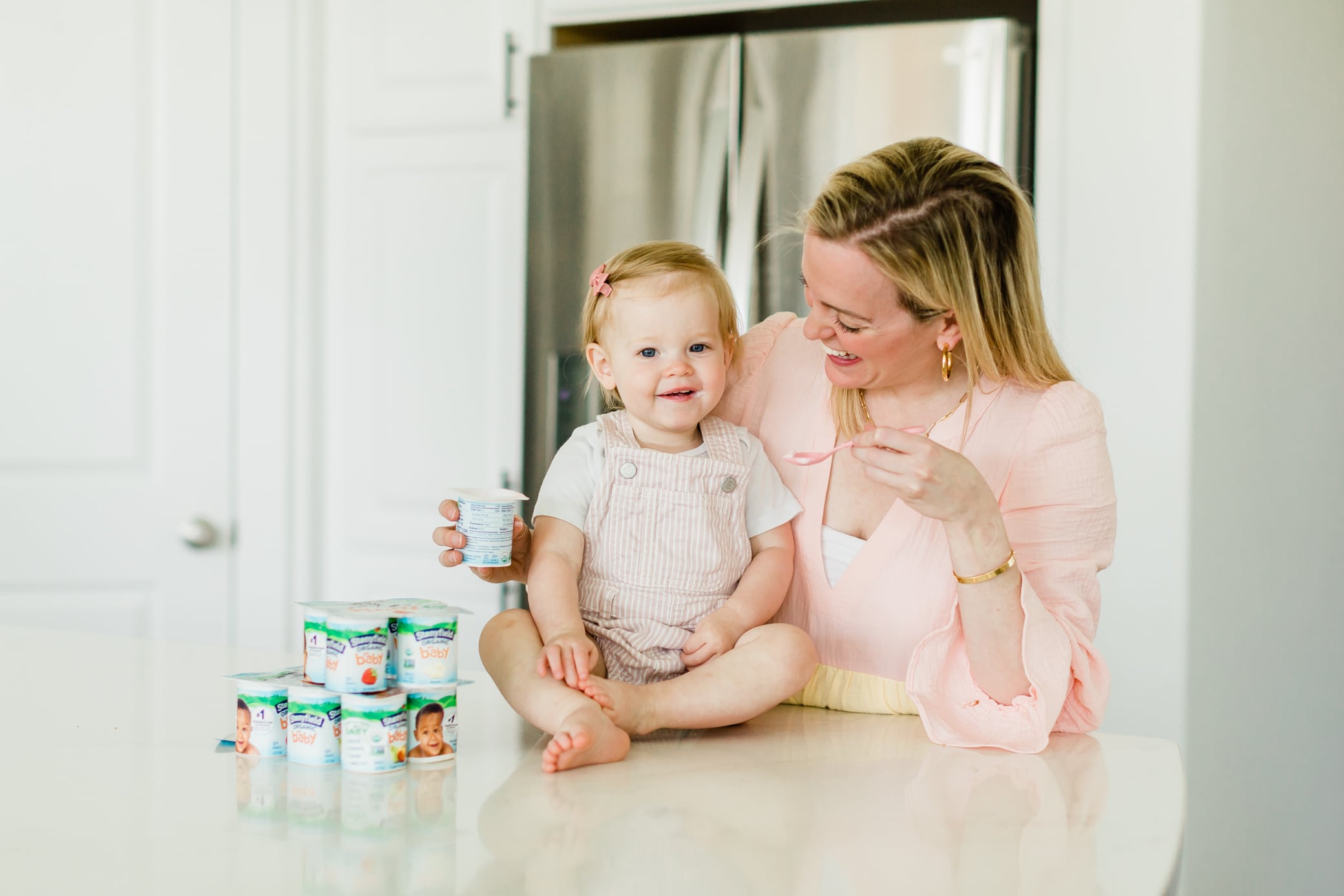 Mom in the kitchen with her baby girl giving her Stonyfield yogurt.
