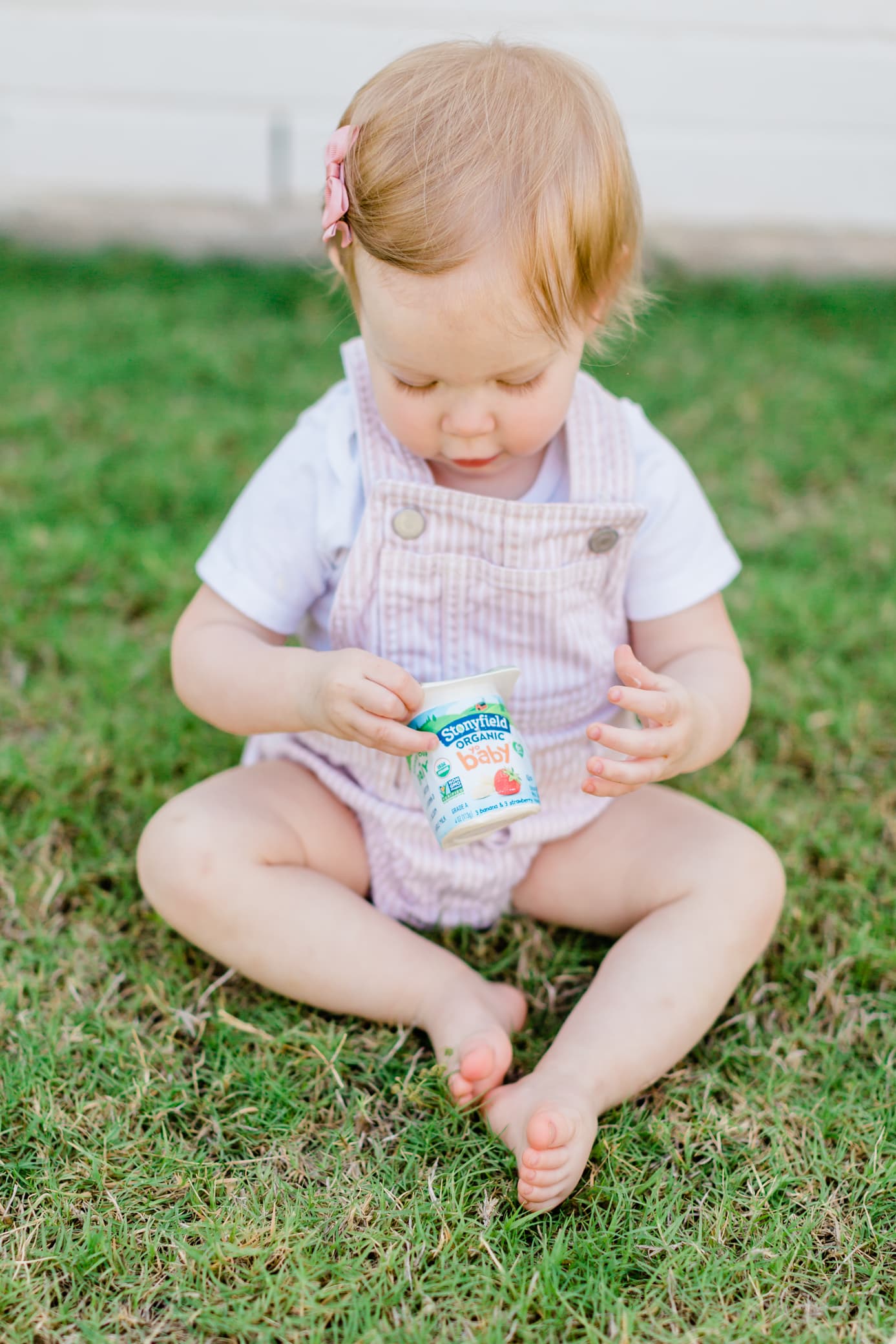 toddler girl sitting outside in the grass holding a cup of stonyfield yogurt