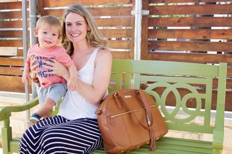 Mom sitting on a bench with diaper bag and holding a young toddler