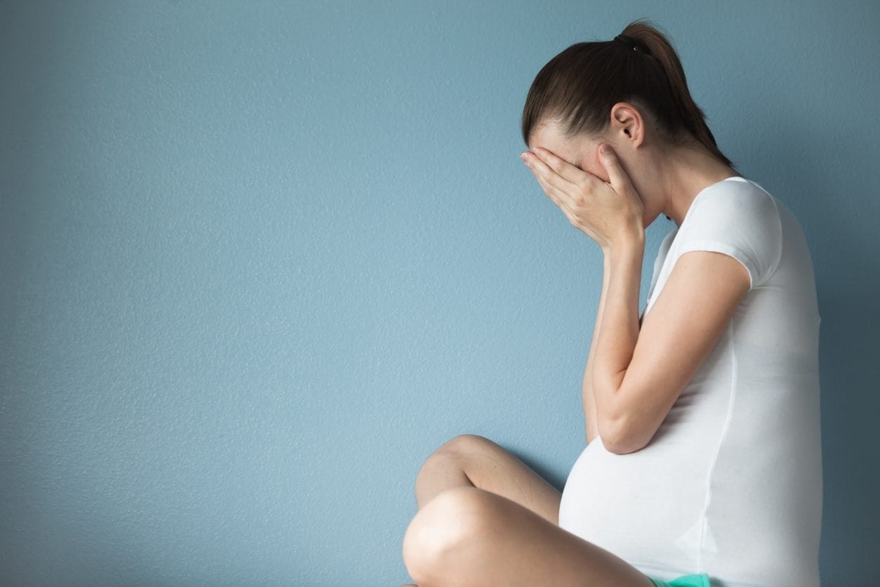 Stressed pregnant woman sitting with her hands on her face.