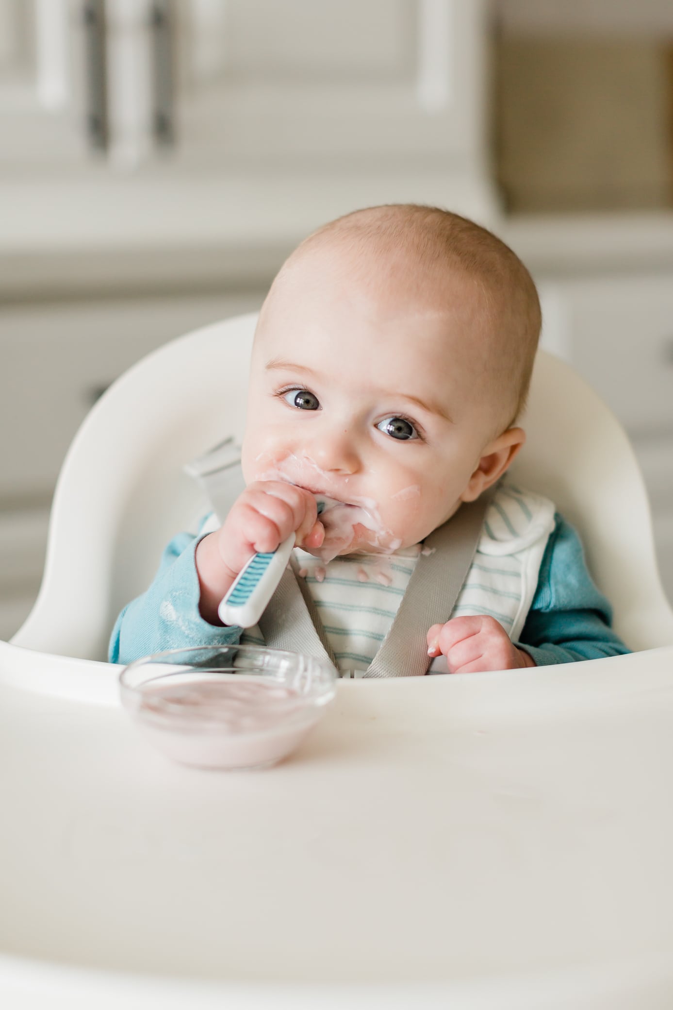 Baby boy sitting in a high chair eating yogurt.
