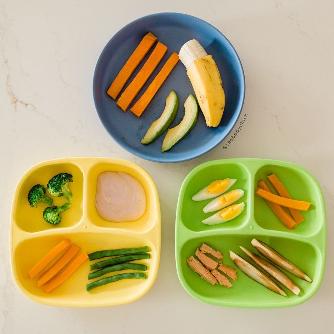 Three toddler plates filled with vegetables, protein, and yogurt.