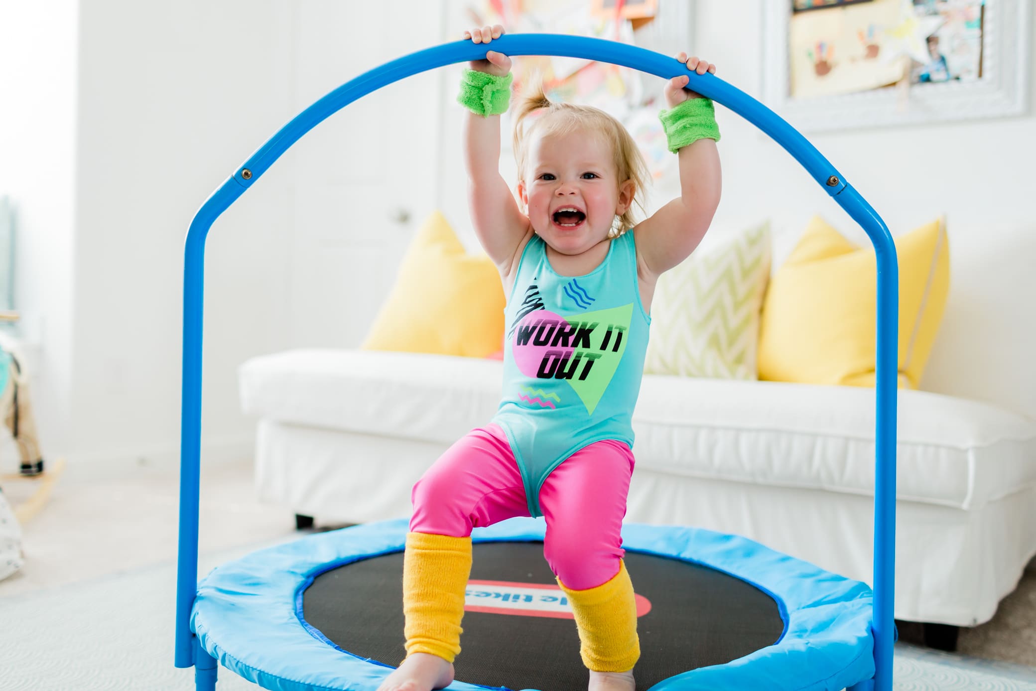 Young toddler girl in a workout outfit jumping on a small kid's trampoline.