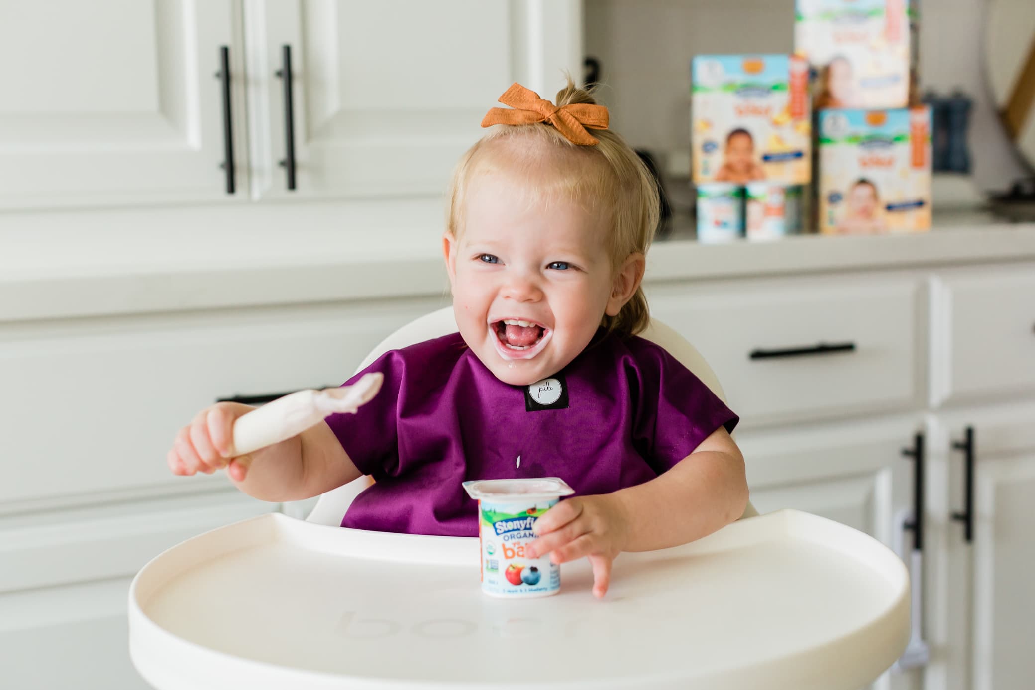 Young toddler girl sitting in her high chair eating Stonyfield yogurt.