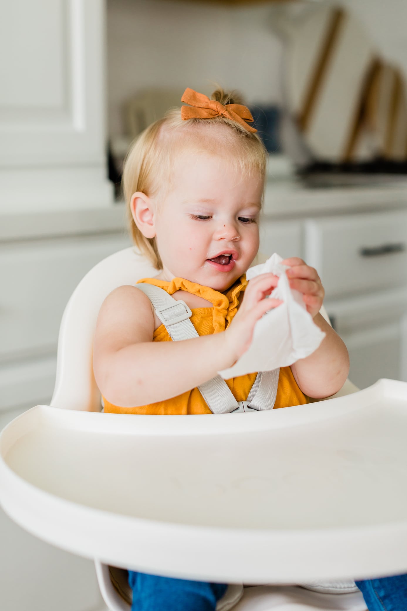 Young toddler girl sitting in her high chair holding a wipe cleaning her hands and her high chair tray.