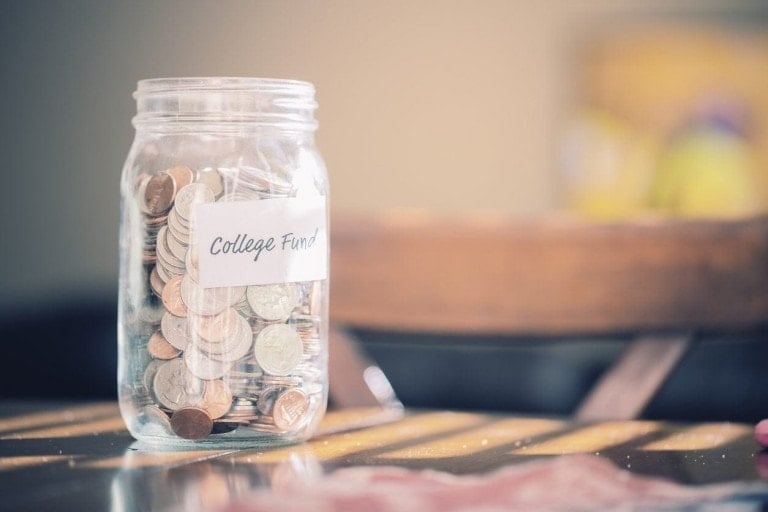 Glass jar labeled college fund filled with coins sitting on table.