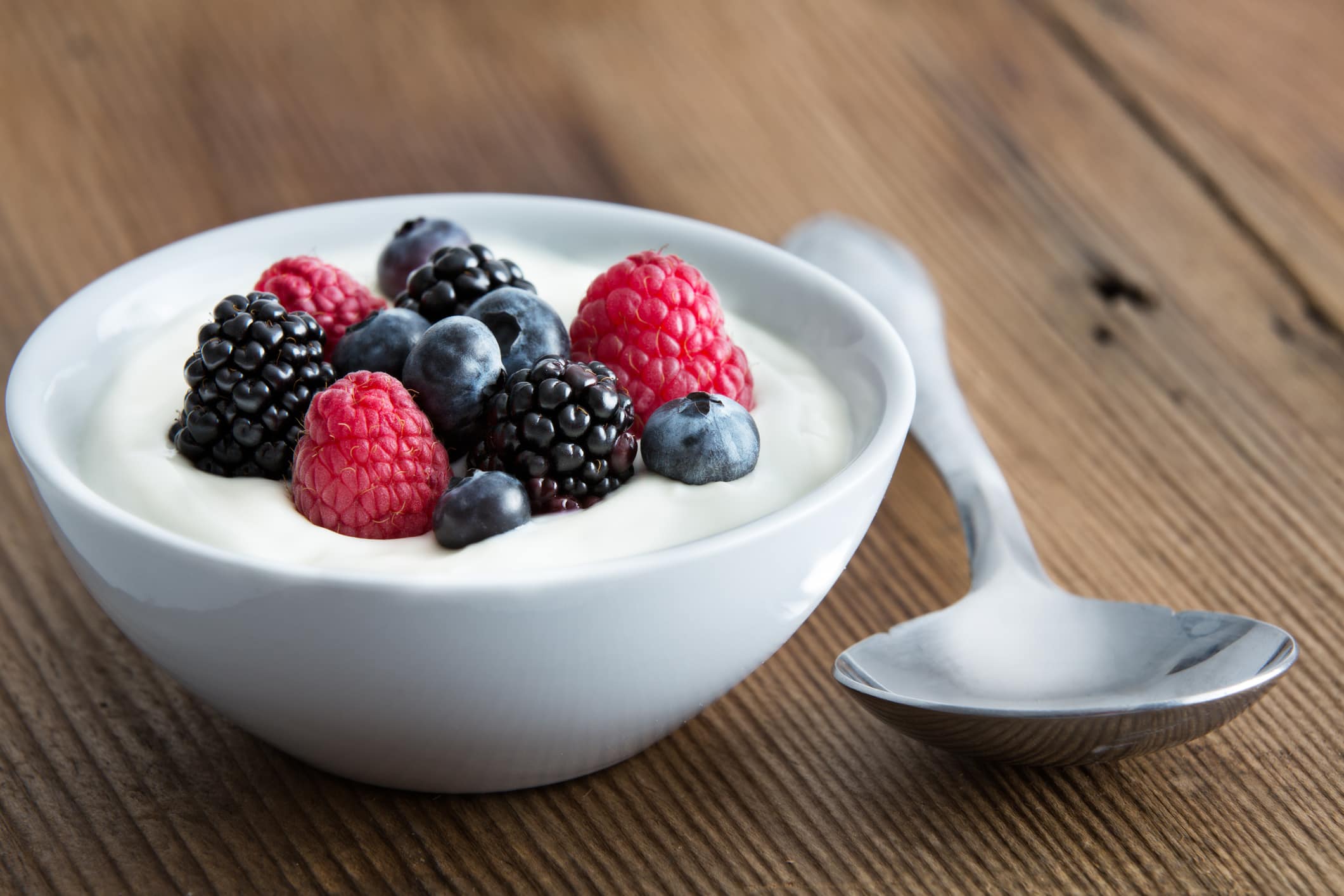 Bowl of fresh mixed berries and yogurt with farm fresh strawberries, blackberries and blueberries served on a wooden table