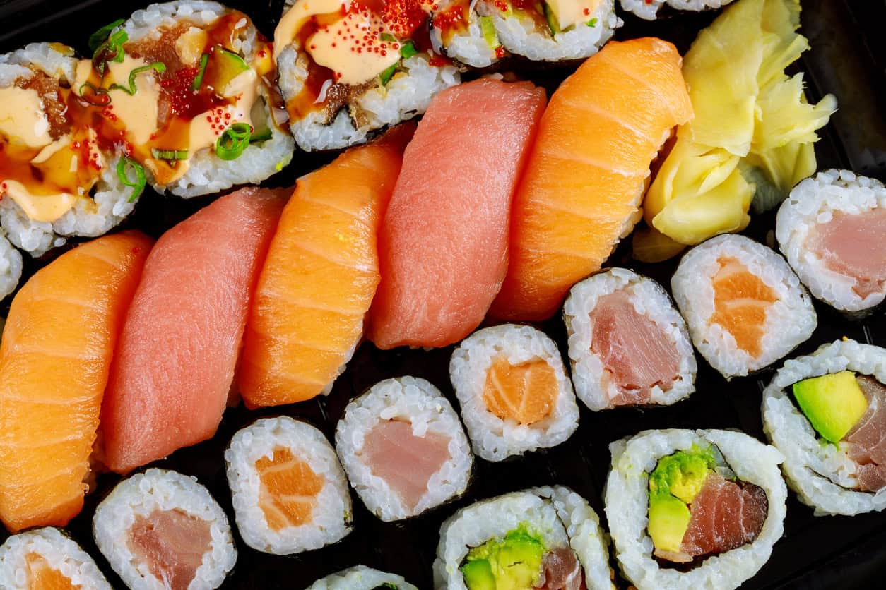 Assorted sushi platter featuring nigiri with salmon and tuna, topped with roe, accompanied by various rolls containing tuna, salmon, and avocado. Garnished with pickled ginger.
