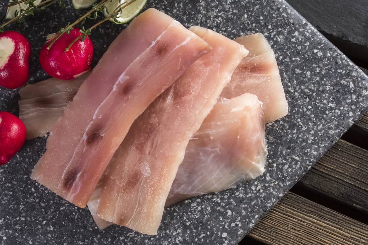 Slices of raw mahi mahi fish grace a gray stone surface, paired with vibrant red radishes and their green stems.