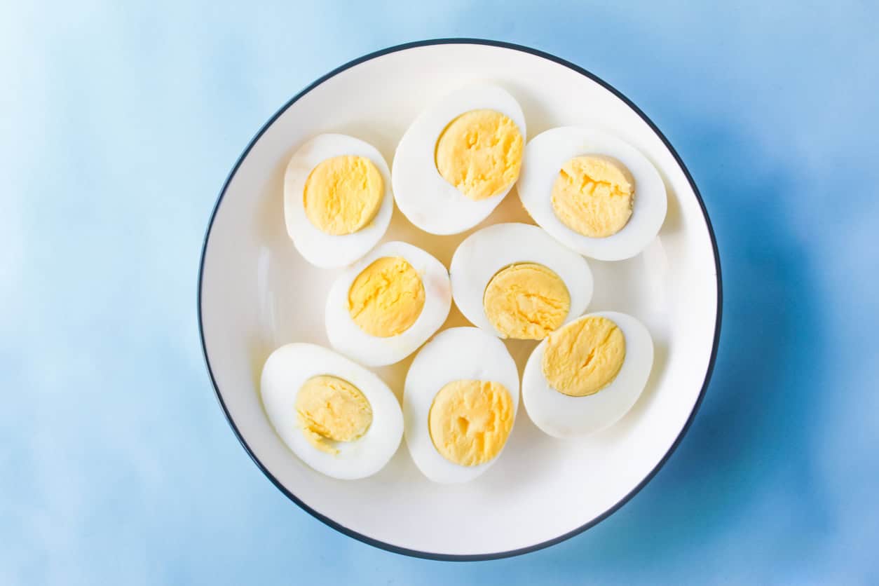 A plate with nine halved hard-boiled eggs, a delicious and healthy snack for pregnancy, is set against a light blue background.