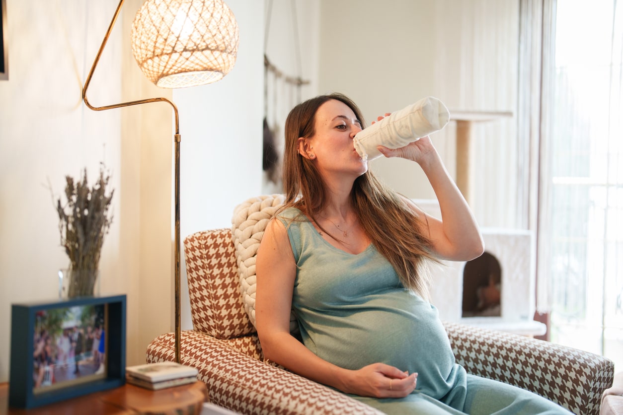 Expectant woman drinking a bottle of water sitting in her hair in living room