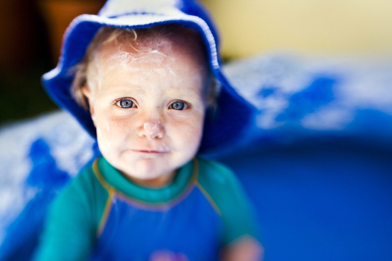 Young baby wearing a blue swimsuit with sunscreen on his face.
