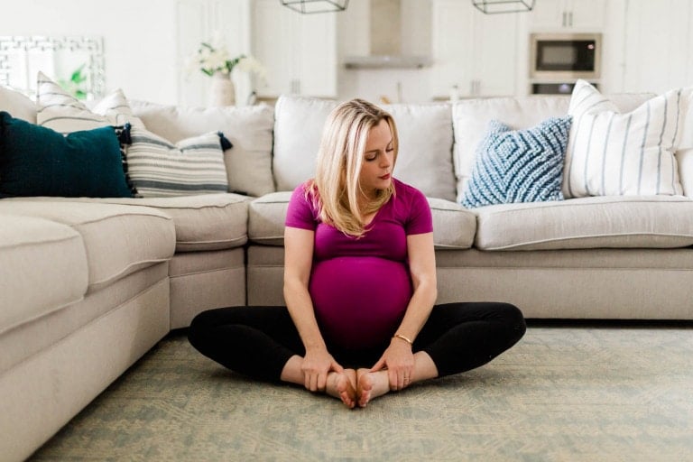 A pregnant woman sitting on the floor doing hip opening stretches.