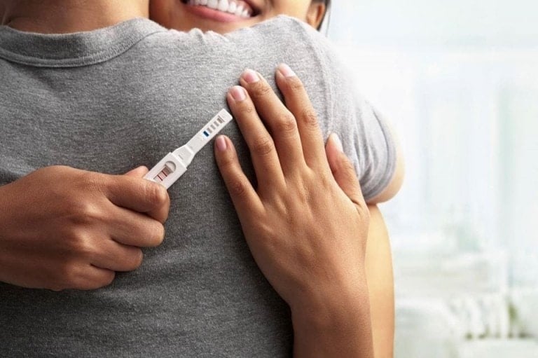 Woman hugging partner with a positive pregnancy test in her hand.