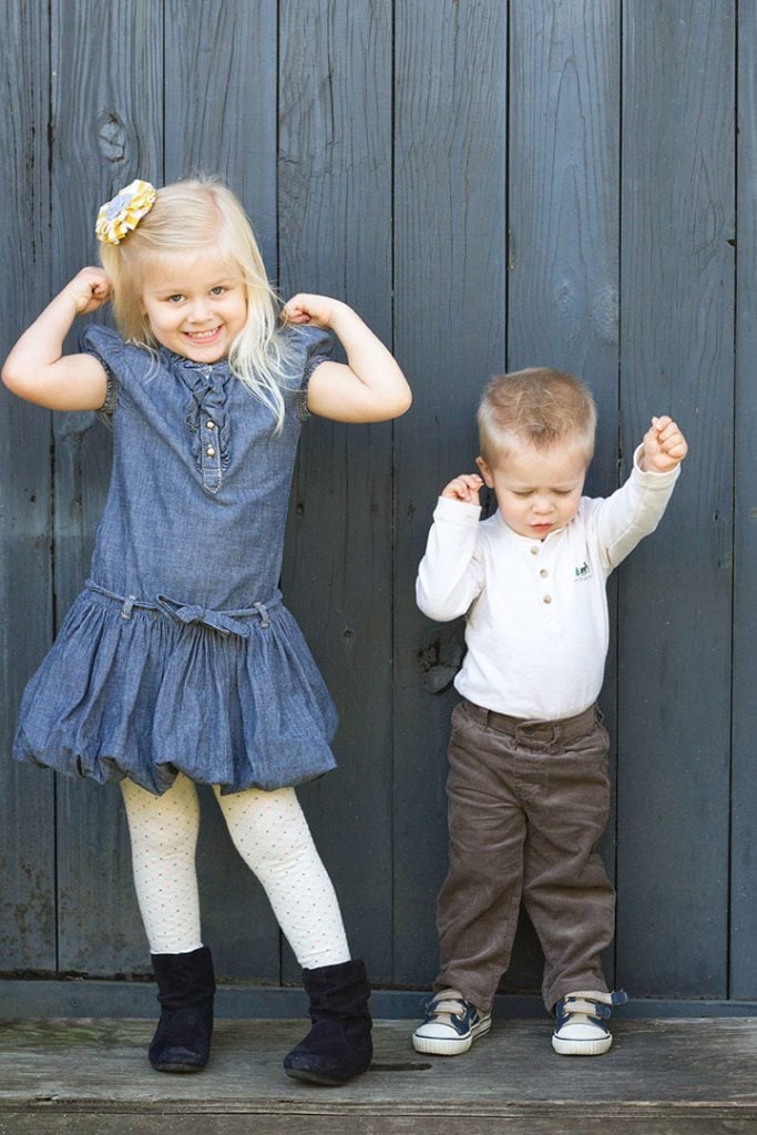 Two toddler aged children (girl and boy) flexing their muscles 