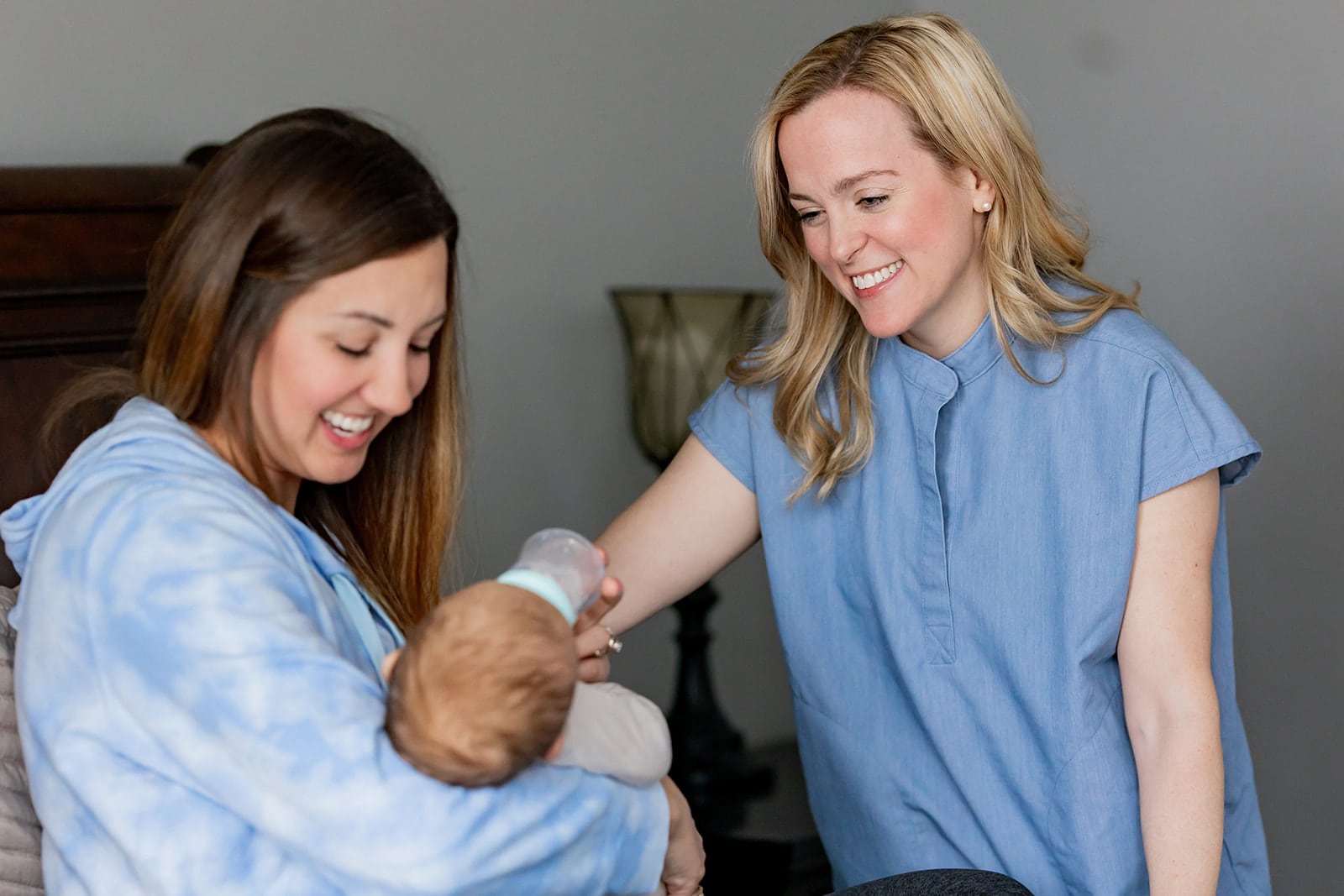 Postpartum doula helping a new mom with her baby as she feeds her baby boy a bottle.