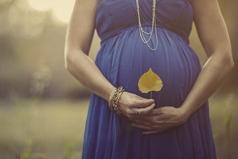 Pregnant woman holding her belly and holding a leaf