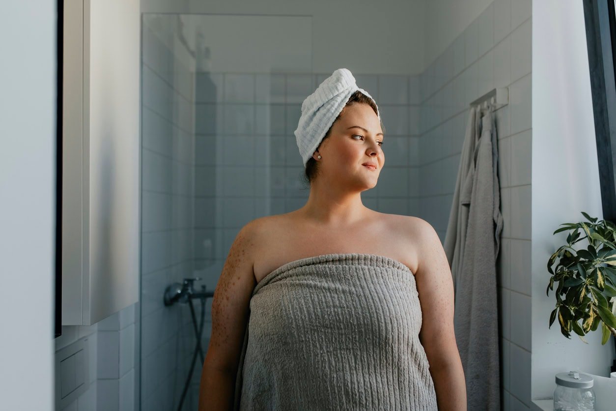 A portrait of a smiling plus size woman standing in the bathroom after having washed her hair.