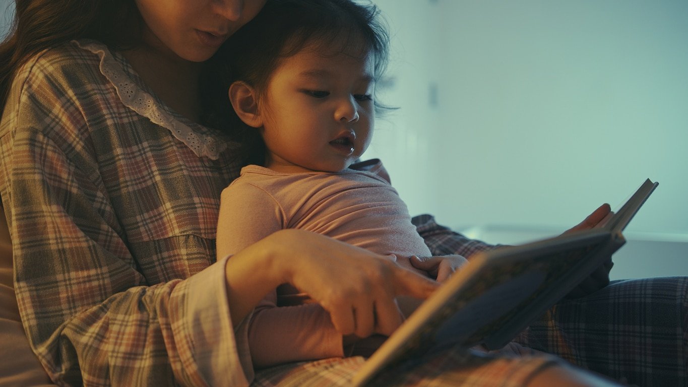 Asian Mother and daughter reading book at home in the bedroom. bedtime story