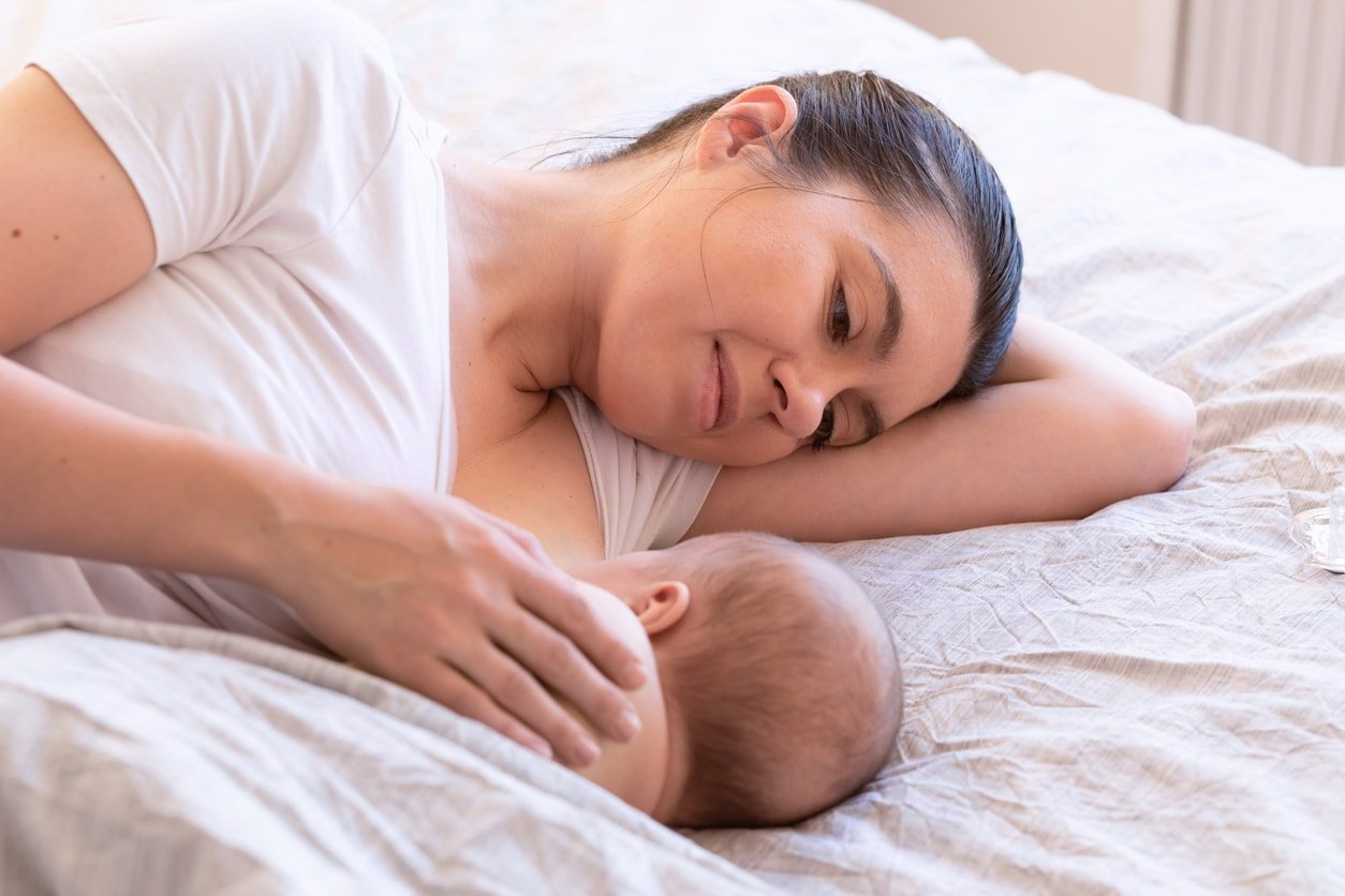 Close-up of mother breastfeeding and hugging newborn baby in a side-lying position. Mom breast feeding her infant baby. Lactation newborn concept. Baby eating milk before sleeping. Mother feed her month son with breast milk