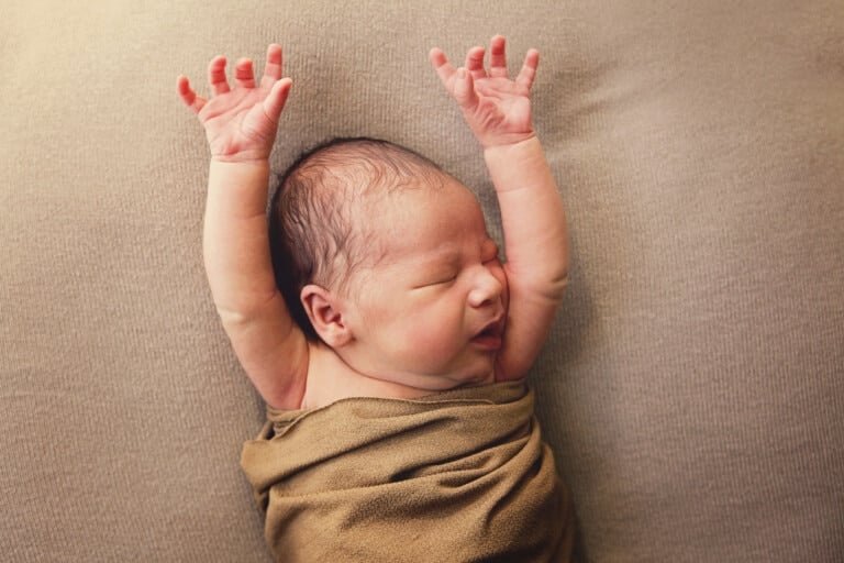 A newborn baby raises his arms over his head for a good stretch. He is eight days old.