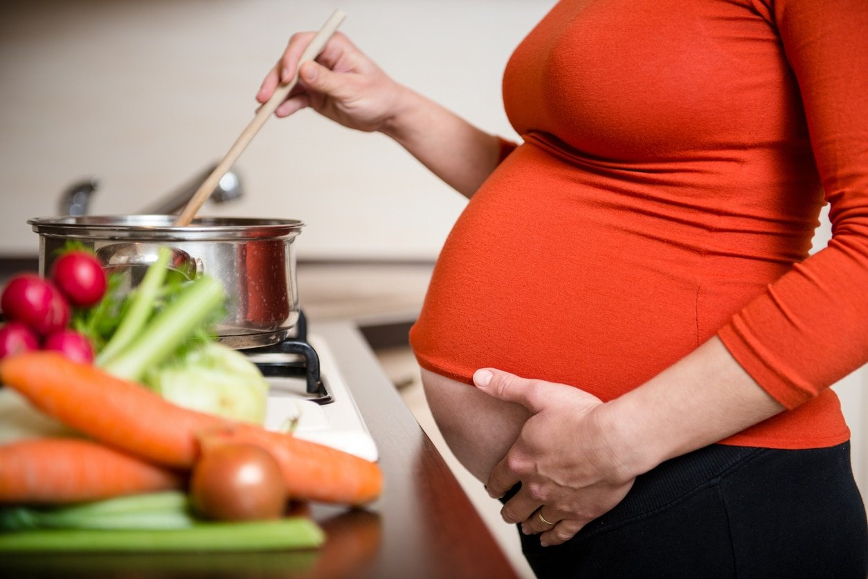 Crop of belly - pregnant woman cooking vegetables in kitchen stirring her wooden spoon in a pot on the stove