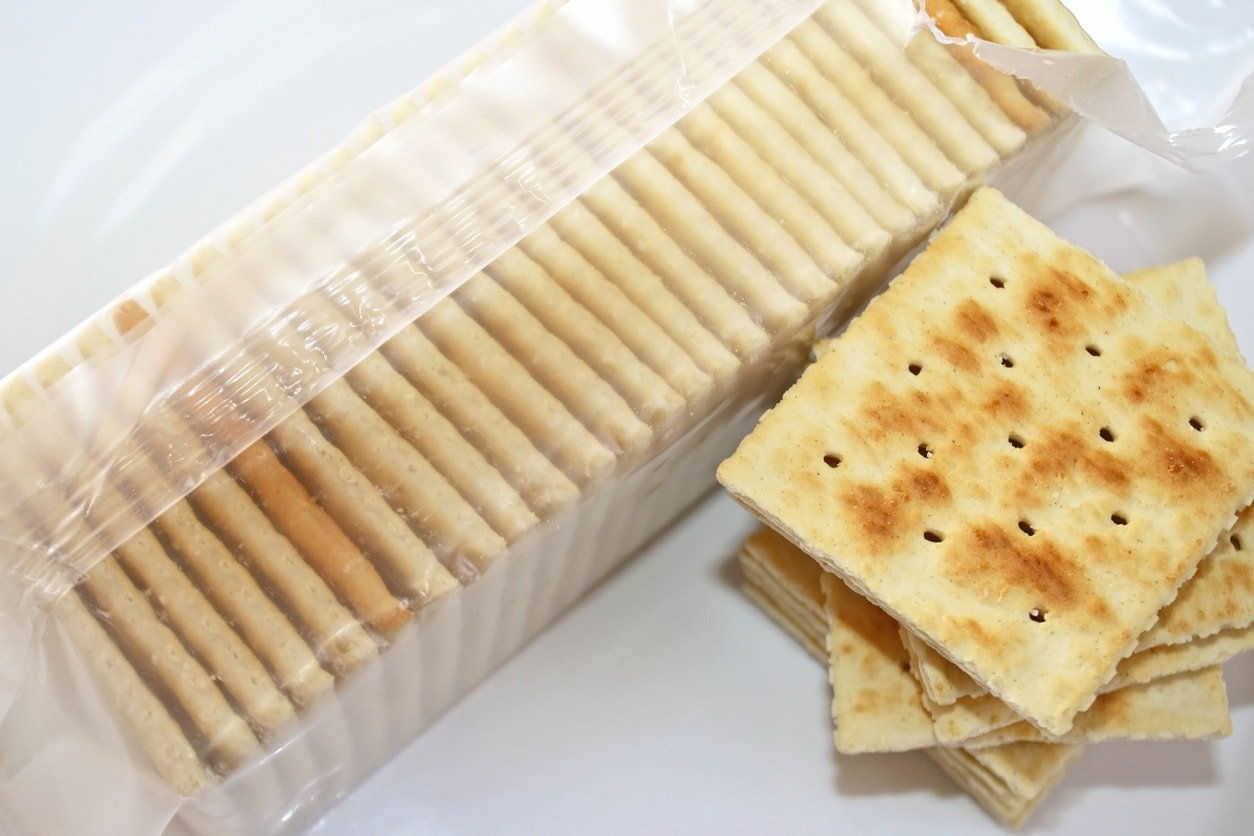 Saltine crackers in a sleeve and sitting next to the sleeve on a white background