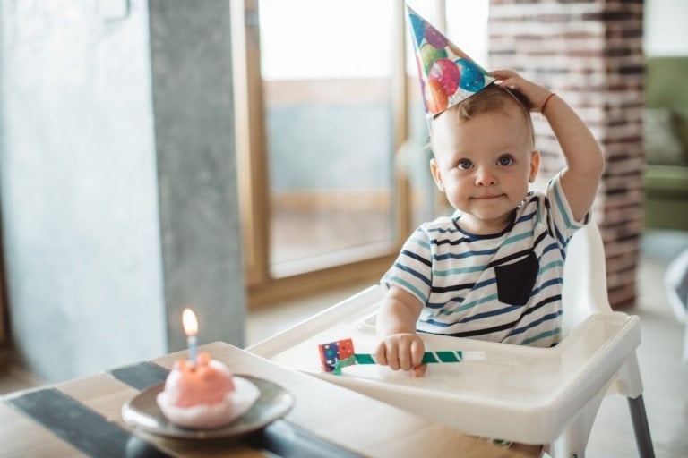 Little boy celebrate first birthday at home, wearing party hats, birthday cake and candle are ready.