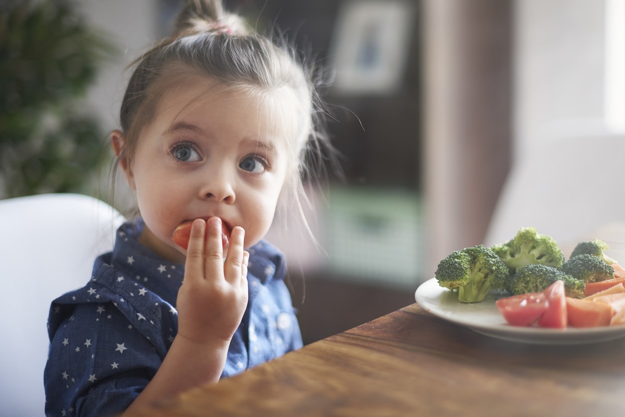 A toddler girl eating vegetables to make her healthier