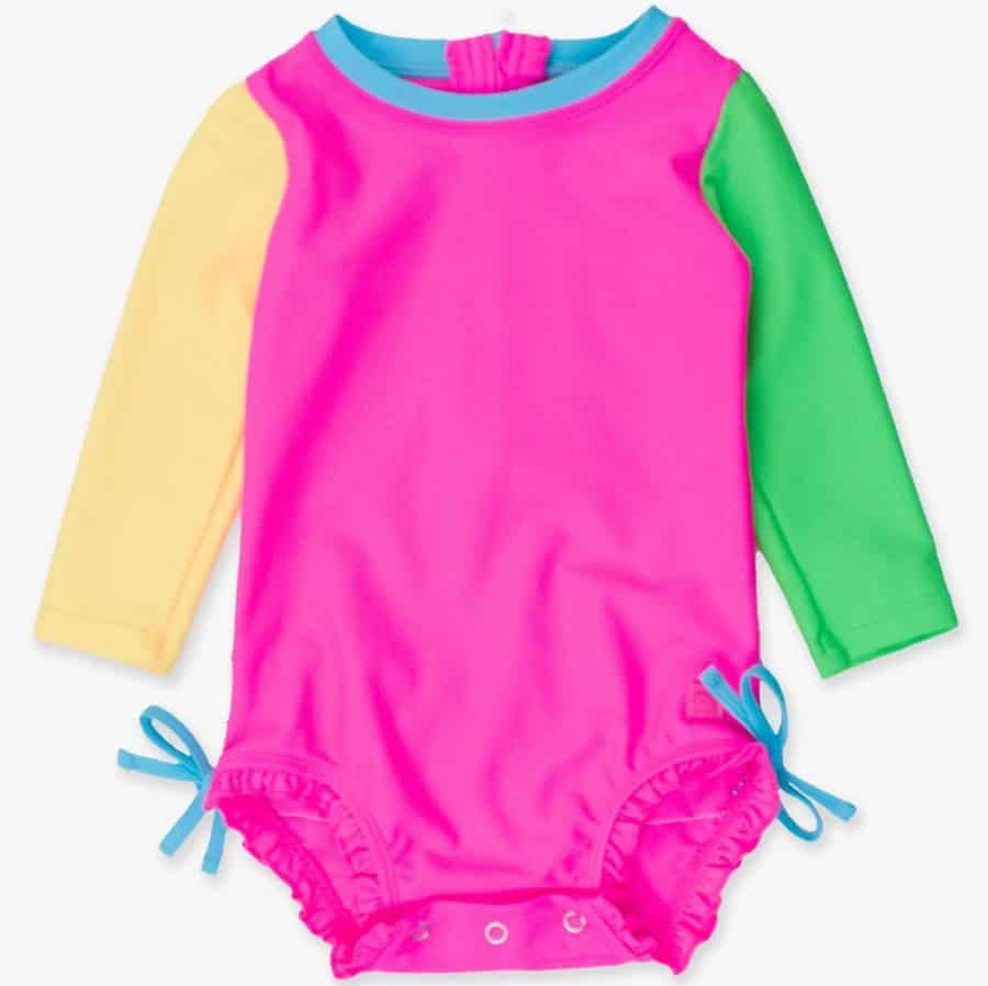 Here is your text with all single quote and double quote characters removed (there actually aren't any in the original text, but here's the text unaltered): A long-sleeve baby swimsuit—one of this season’s summer must-haves—with a bright pink body, yellow left sleeve, green right sleeve, blue neck trim, side ties at the hips, and convenient snap closures at the bottom.
