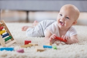 Cute baby sings with open mouth while playing with wooden blocks.