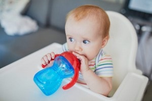 Little baby girl sitting in high chair drinking water from her sippy cup.