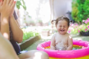 one year old baby girl is playing , splashing in the pool . baby is first time in pool and she is very happy and excited. mother is sitting beside her