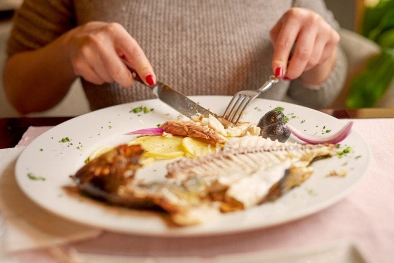 woman in restaurant eating fish, plate in front of her.