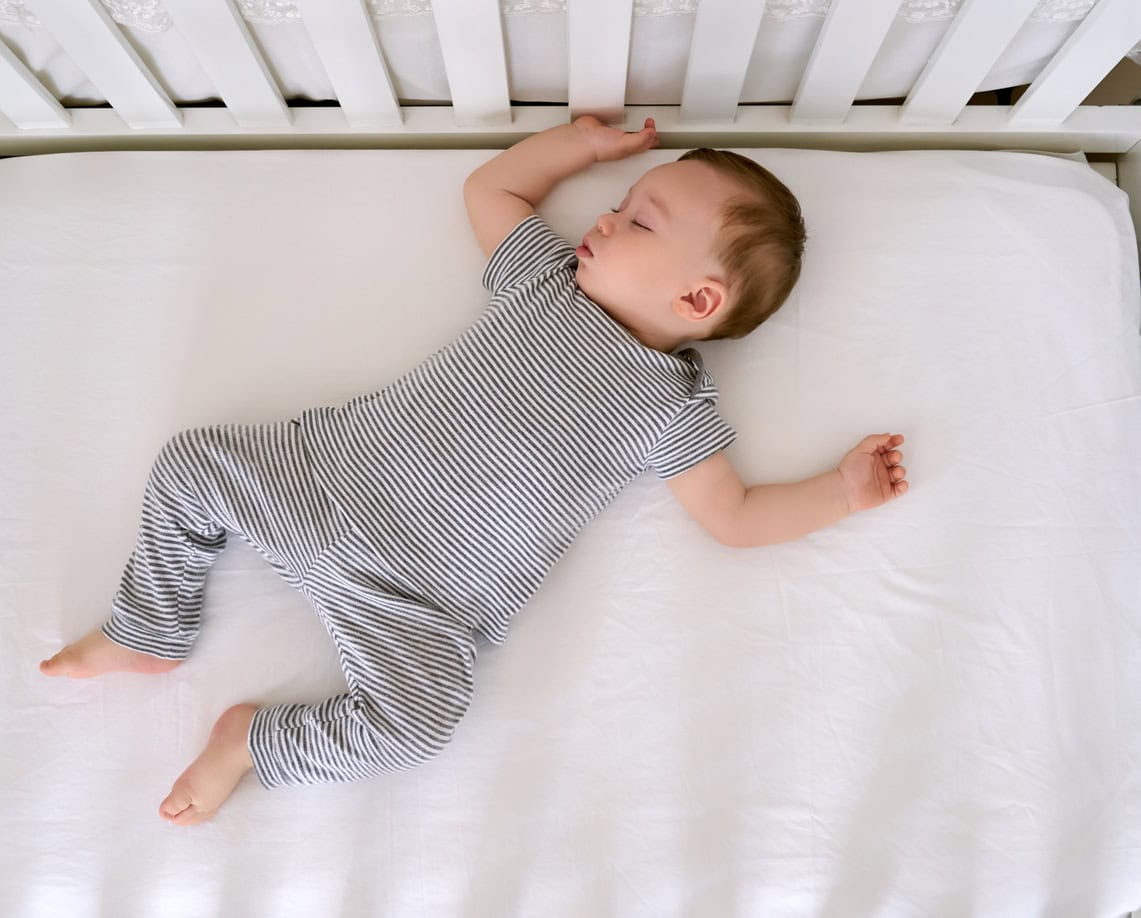 Cute baby is sleeping on his back in his crib