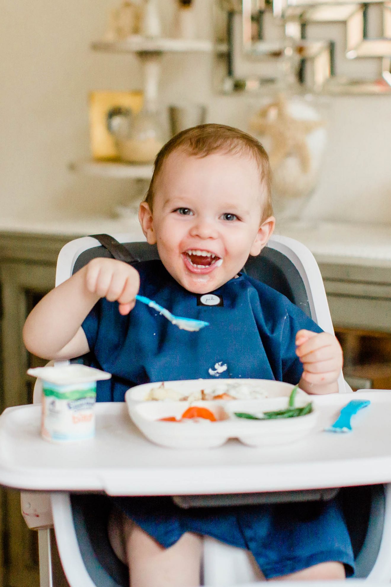 Happy toddler boy enjoying his meal sitting in his highchair.